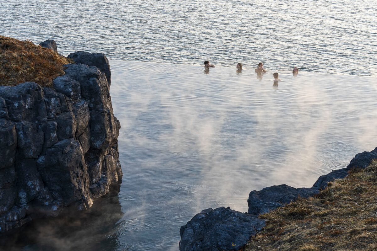 People soaking in a steaming infinity pool next to the ocean.