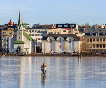 People ice skating on a frozen lake with a city skyline behind.