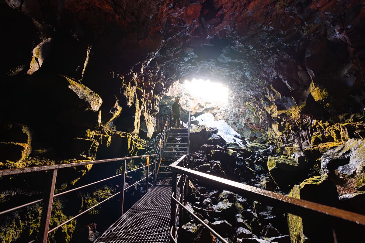 A person walking up metal stairs inside a volcanic cave.