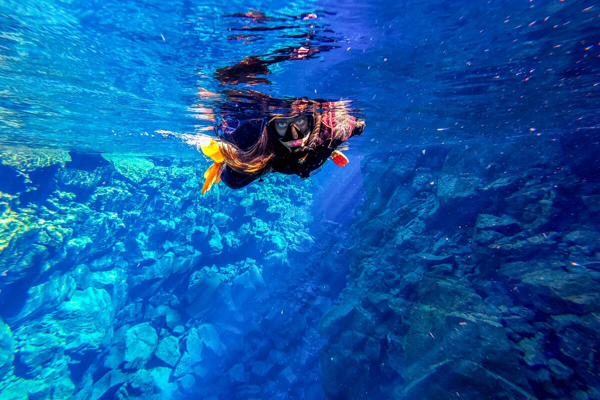 A diver snorkeling between two rocky underwater cliffs.