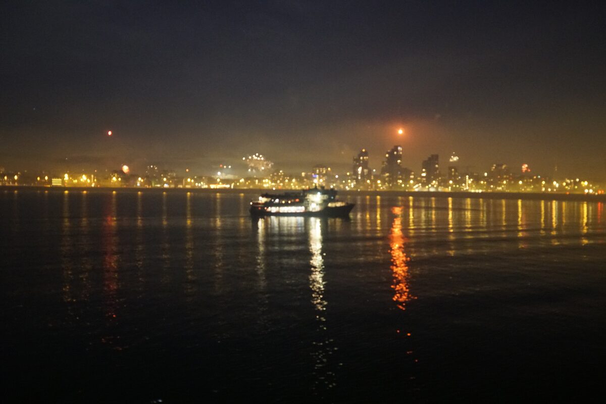 Lit boat on water with city skyline background at night.