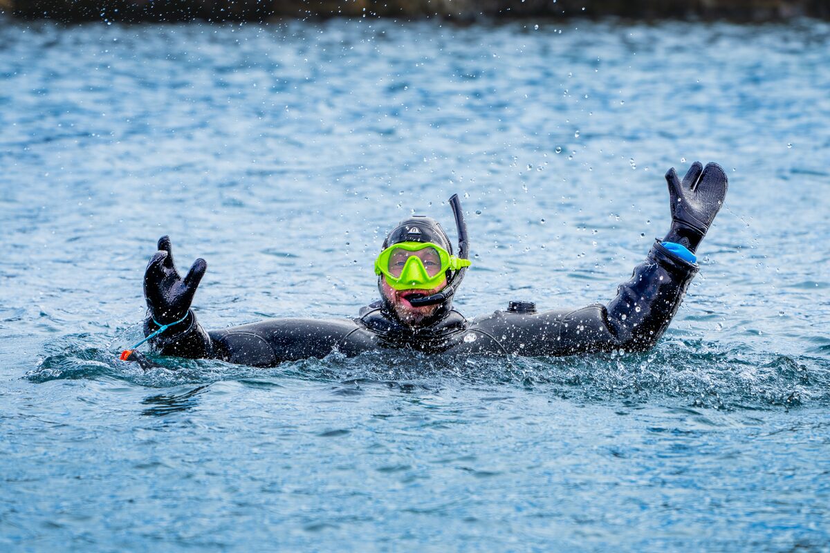 A diver in a wetsuit emerges from water with arms raised.