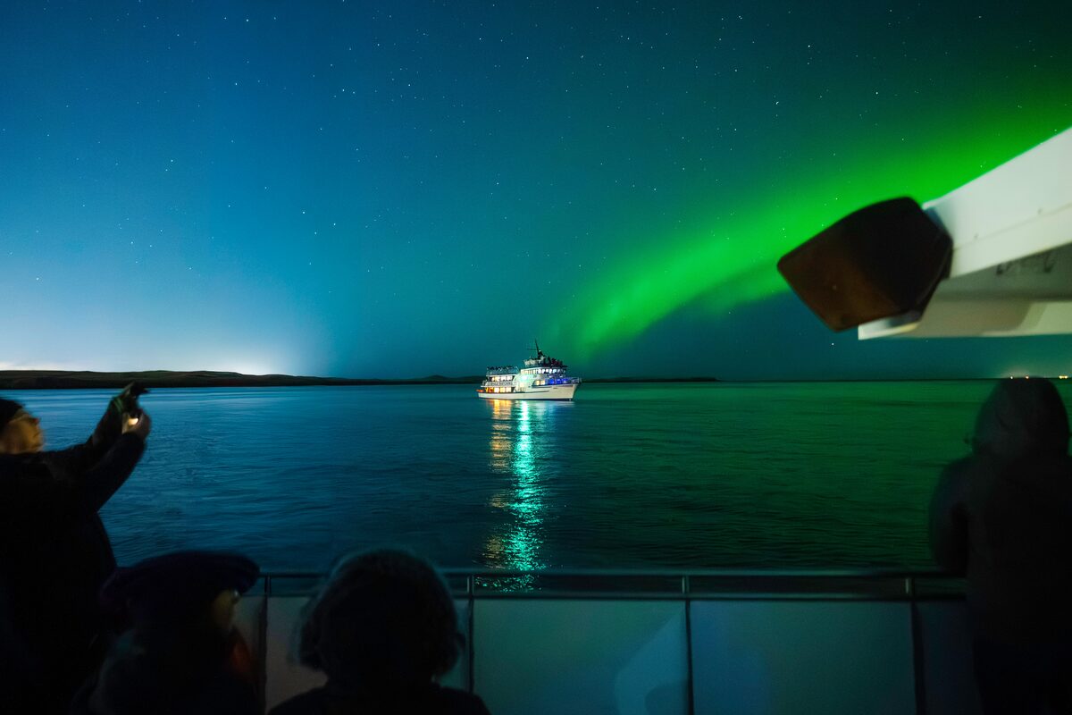 Tourists watch northern lights from a boat at night.