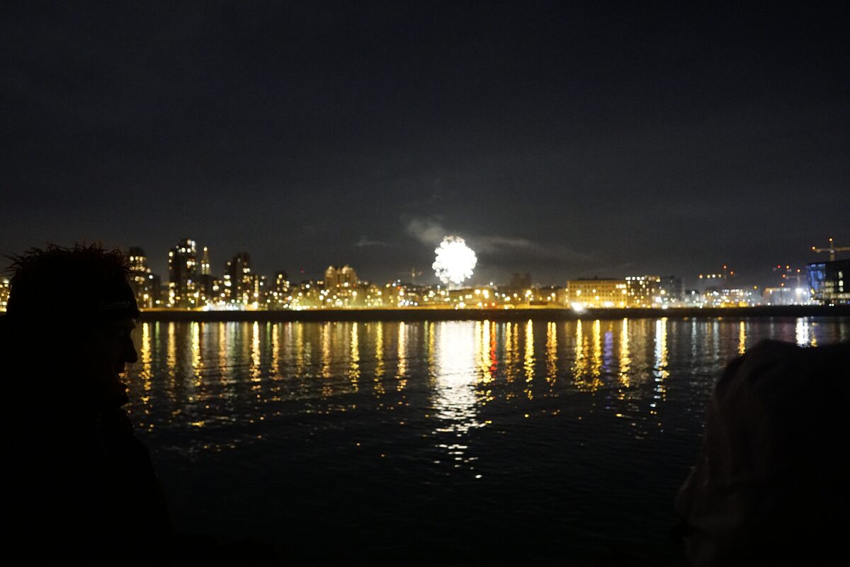 City skyline with fireworks reflecting on water at night.