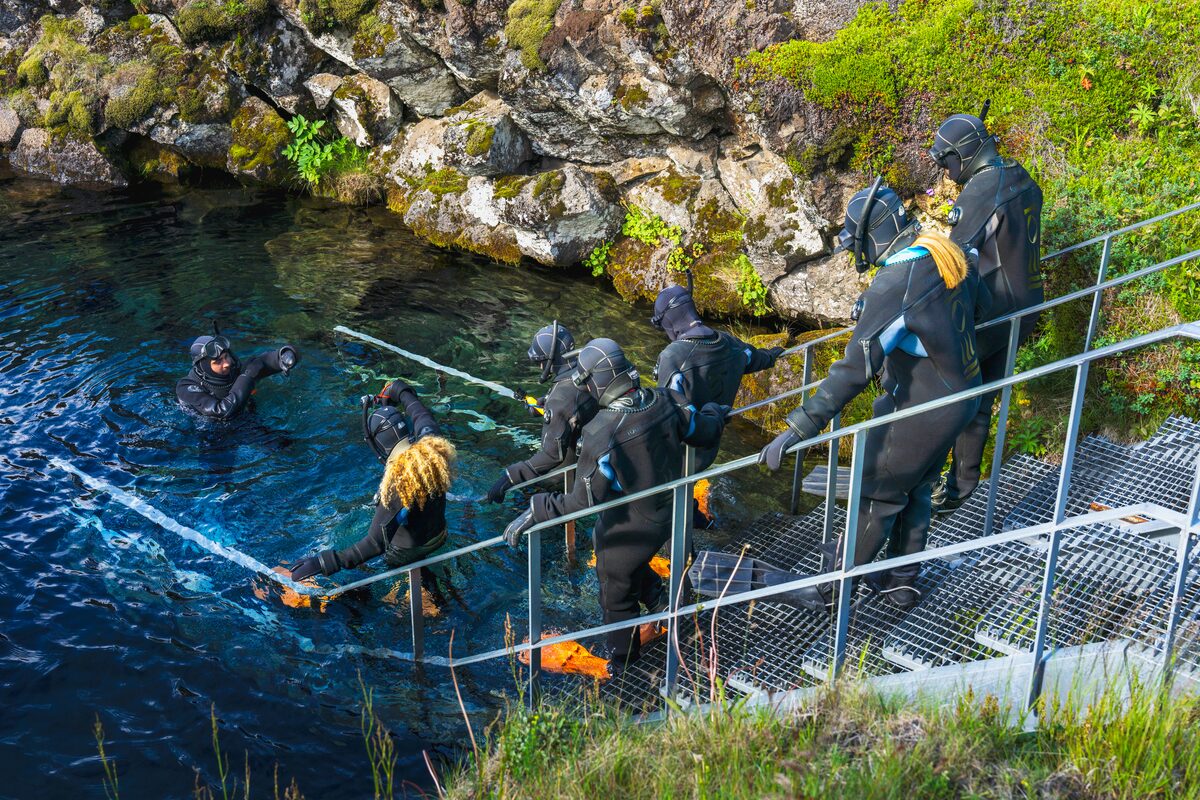 Divers descending stairs into a clear water body.