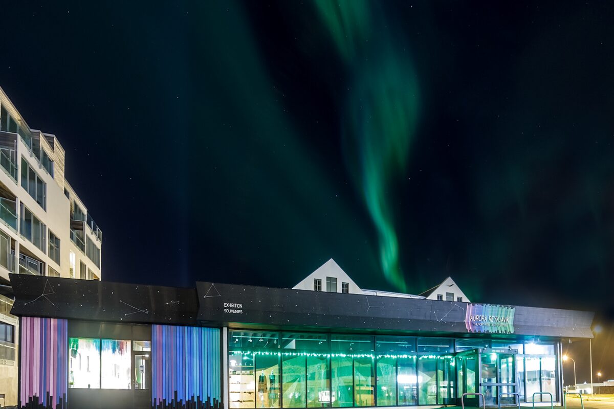 Aurora borealis glowing in the night sky over a building in Reykjavík, Iceland.