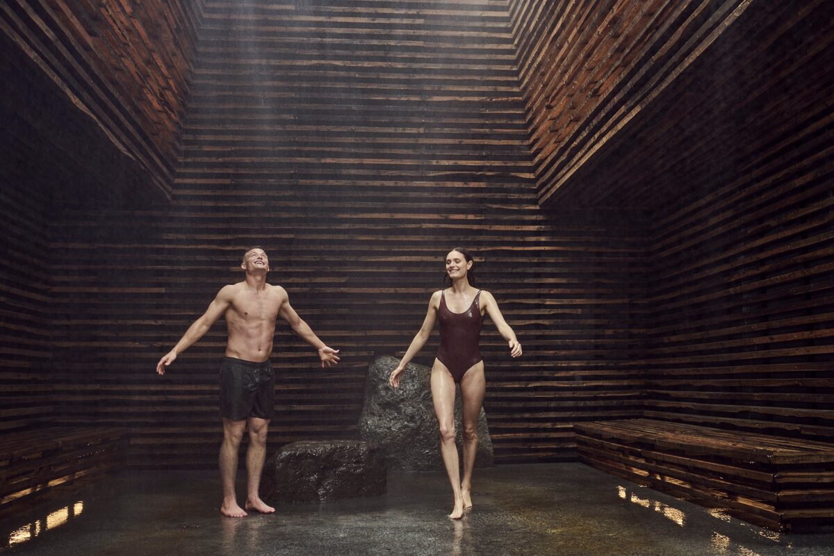 A man and a woman in a rustic, slatted wooden room.