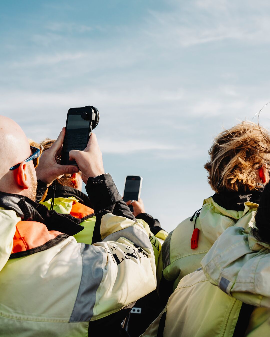 A group of people wearing jackets holding phones up.