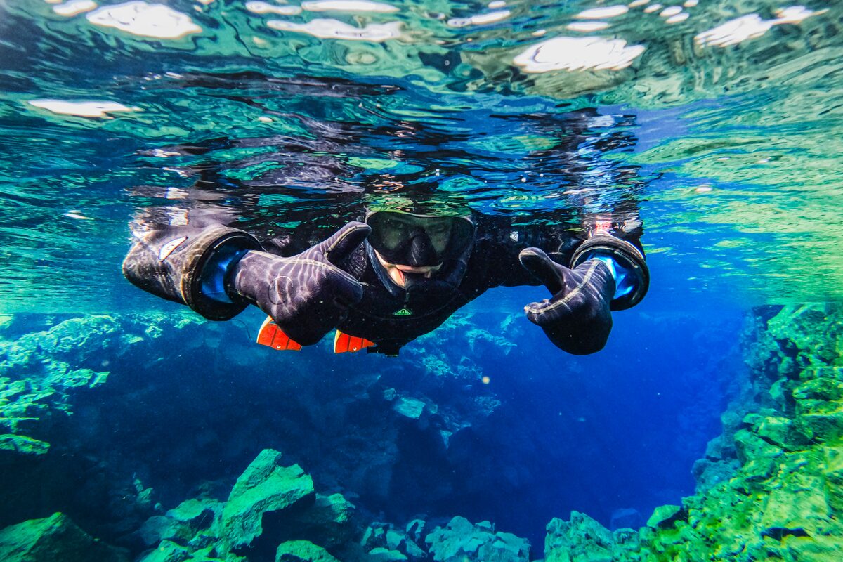 A diver in clear blue water making hand gestures.