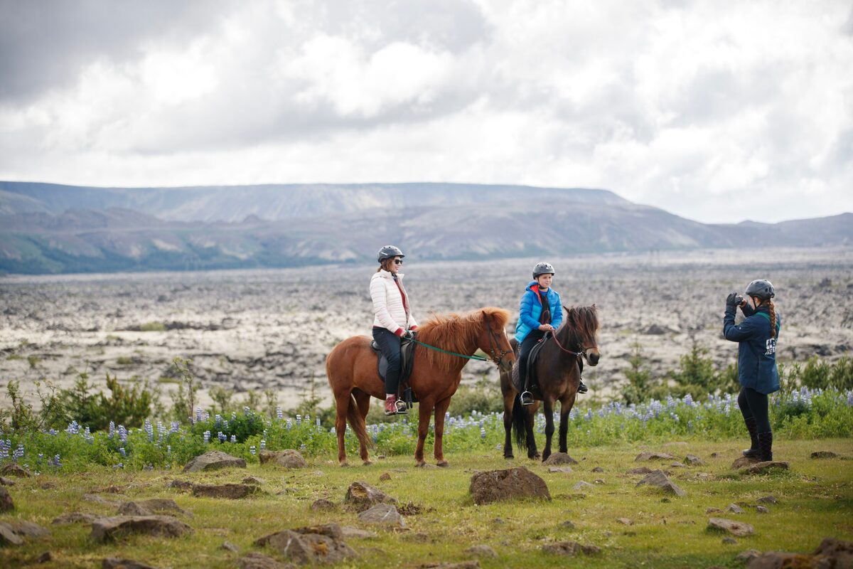 Two people horseback riding while another takes pictures.