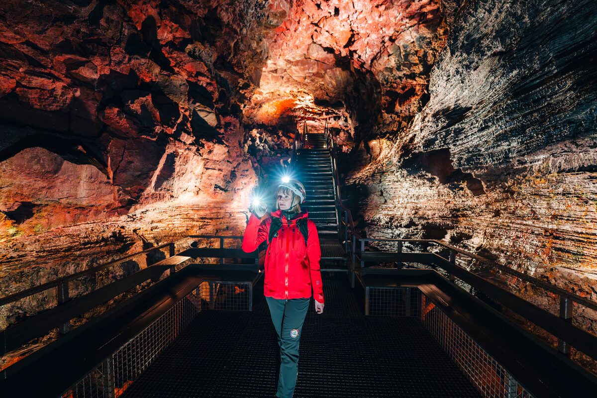 A woman walking inside a lava cave holding a flashlight.