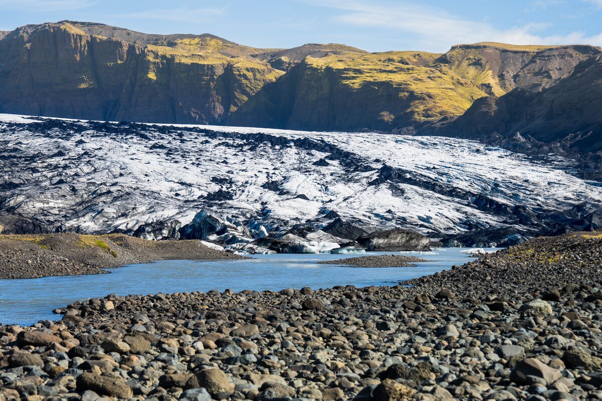 Glacier with rocky foreground and mountains in background