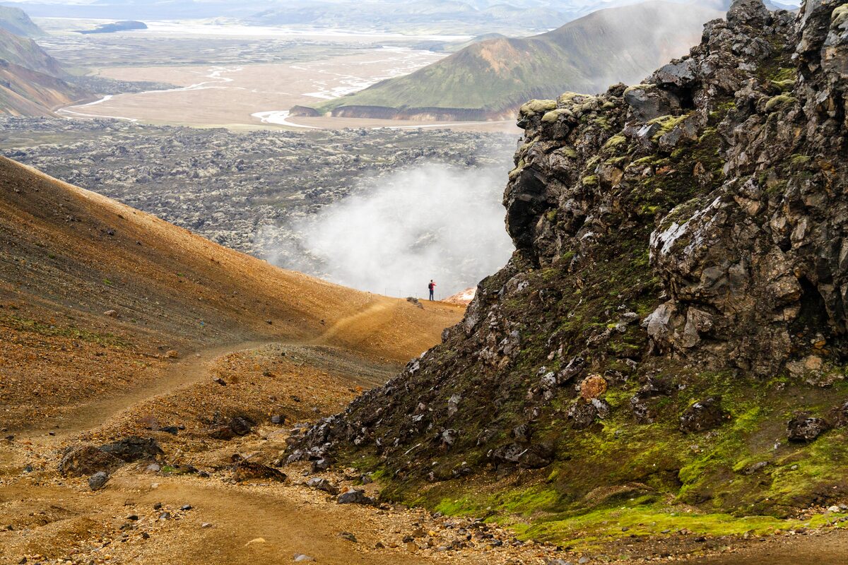 Hikers on a trail in a volcanic landscape with steam vents.