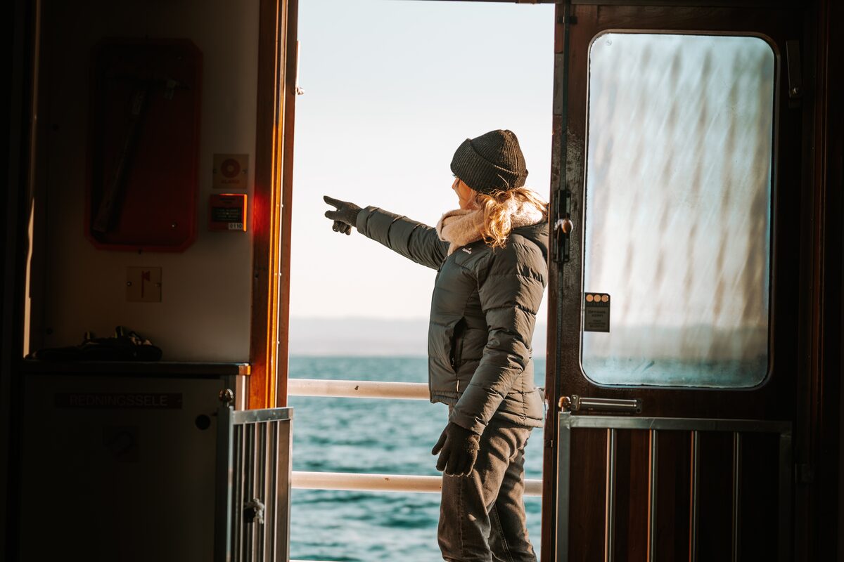 A woman pointing outside from a boat door.