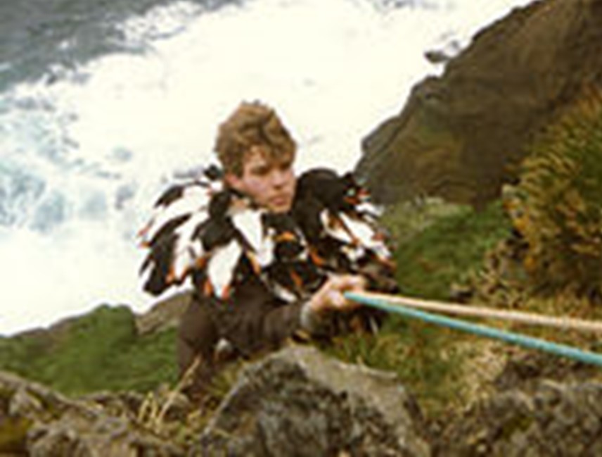 A man clinging to a rocky cliffside by ropes.