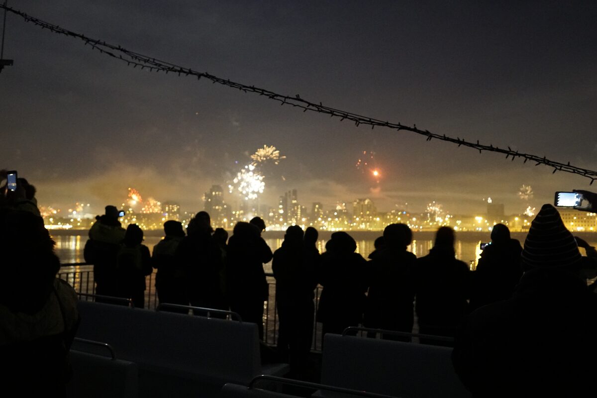 Silhouettes of people watching fireworks over a city.
