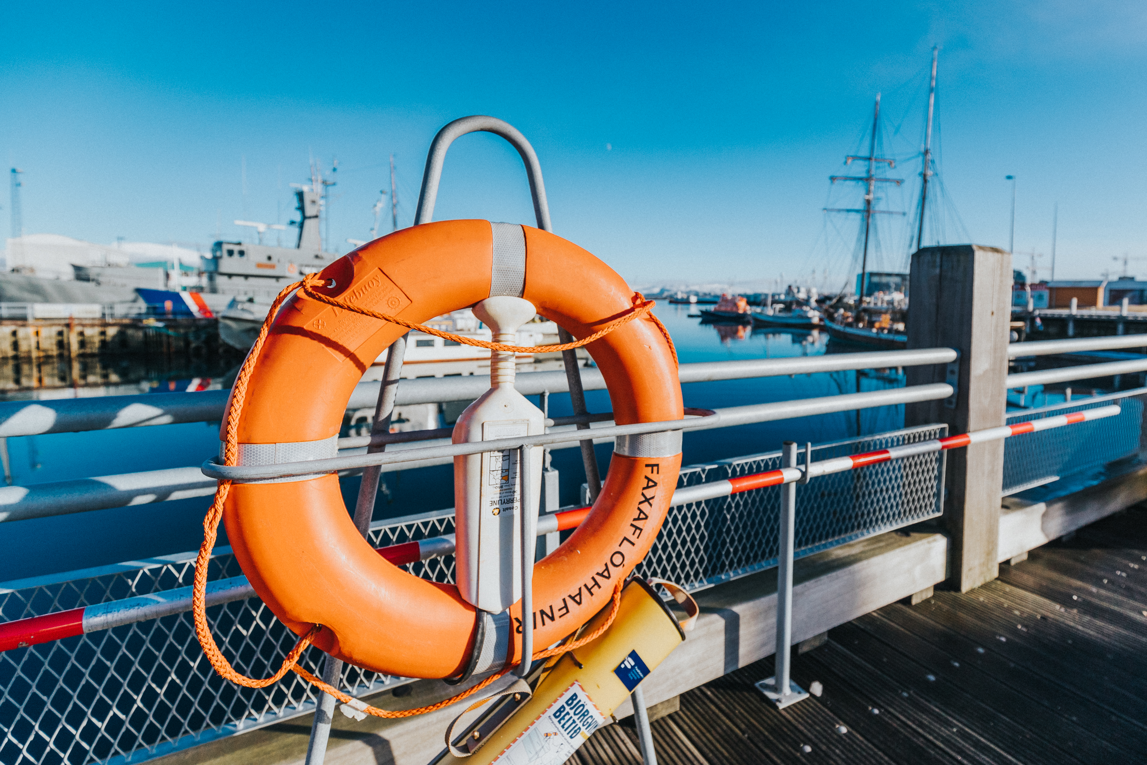 Orange life ring on a harbor pier with docked ships.