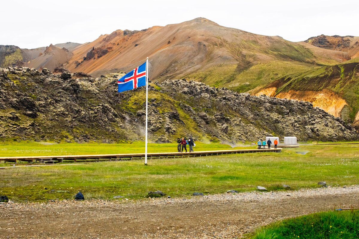 An Icelandic flag in a mountainous landscape with hikers.