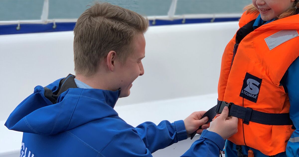 Man helping child put on life jacket on a boat.