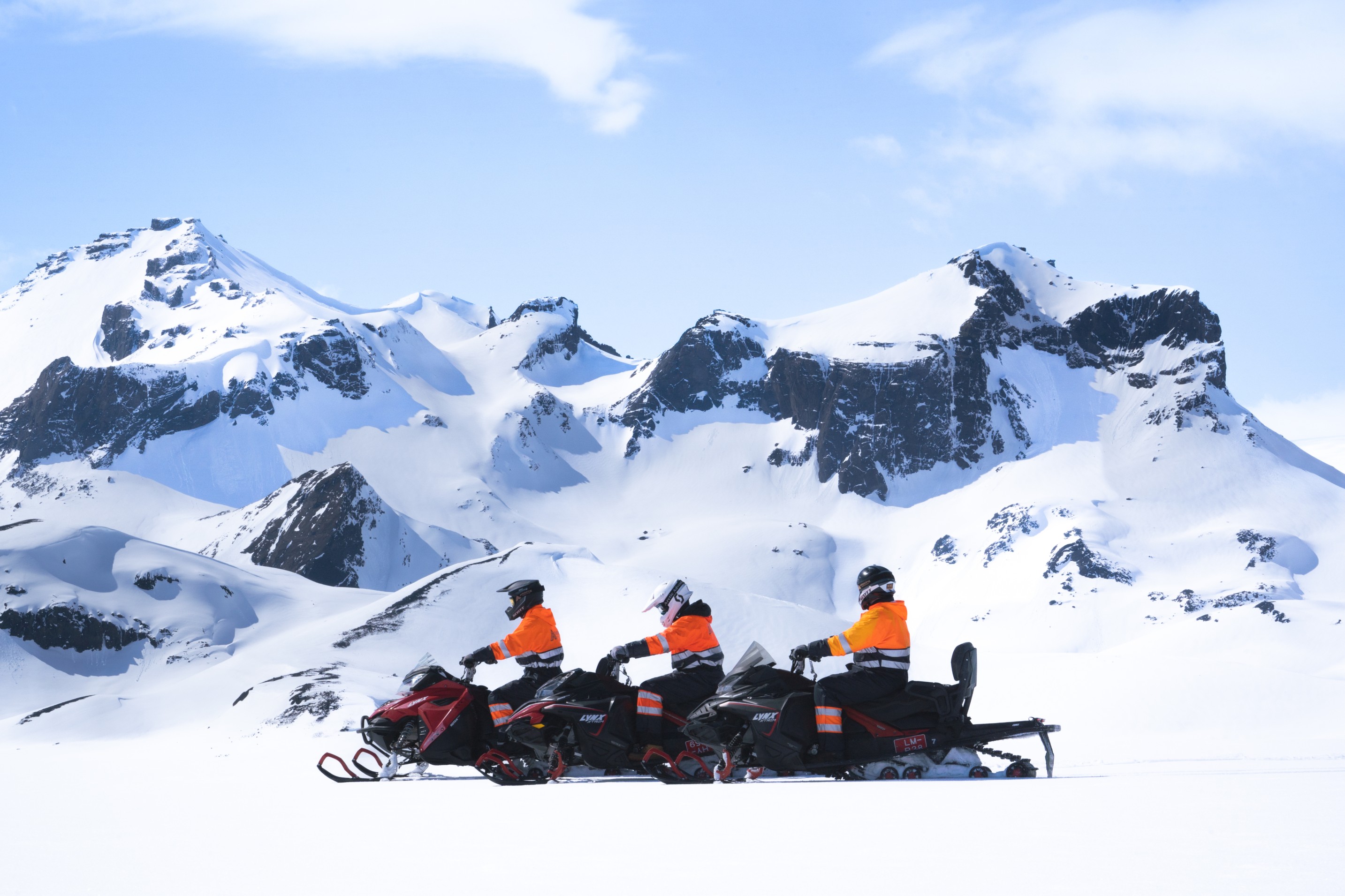 Three people on snowmobiles in a snowy mountain landscape