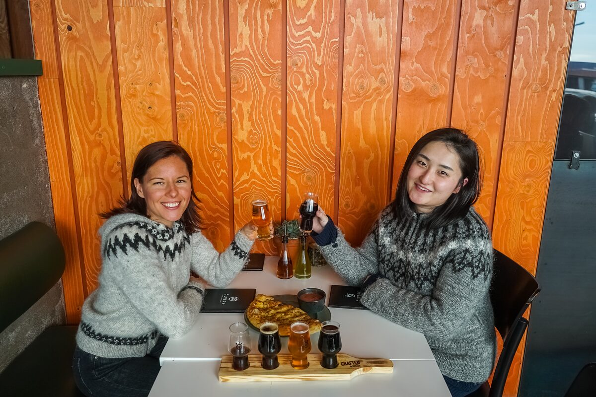 Two women in sweaters sharing beers and food.