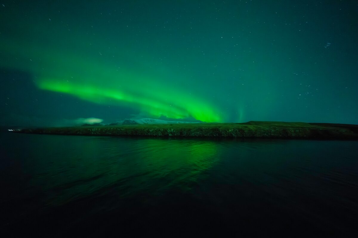 Green northern lights illuminating a night sky over water