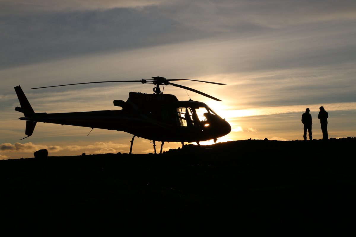 Helicopter silhouetted against a sunset with two people nearby